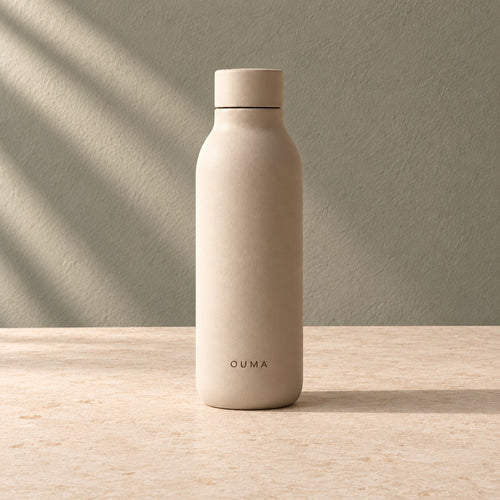Beige OUMA reusable bottle on pale limestone against a sage-grey wall — AI-generated product concept.