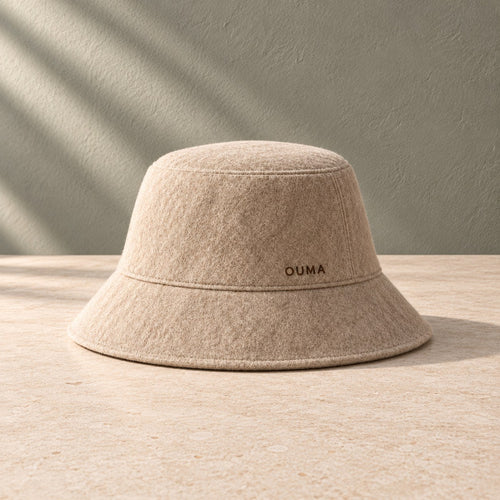 Beige OUMA sauna hat on pale limestone against a sage-grey wall — AI-generated product concept.