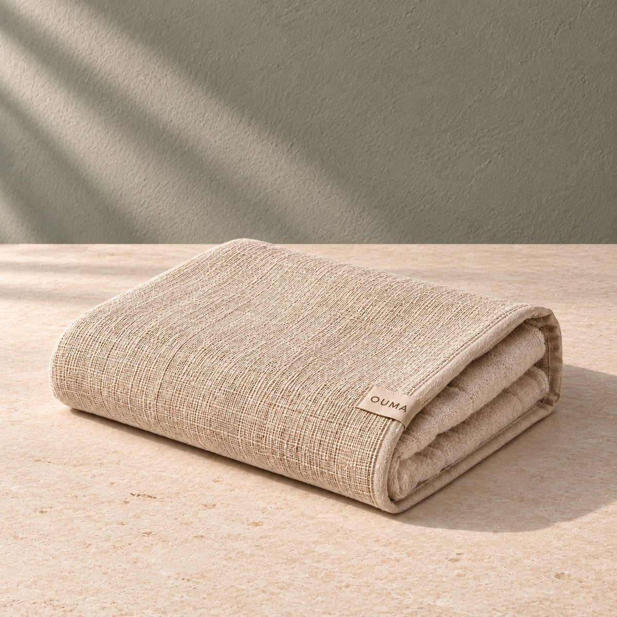 Beige OUMA sauna towel on pale limestone against a sage-grey wall — AI-generated product concept.