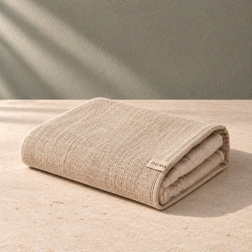 Beige OUMA sauna towel on pale limestone against a sage-grey wall — AI-generated product concept.
